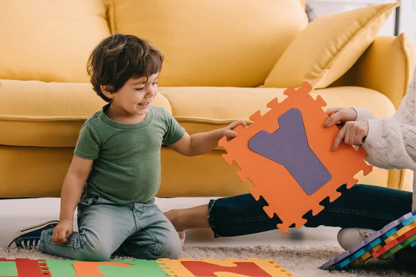 Cropped view of mother and son playing with alphabet puzzle mat on carpet — Stock Photo