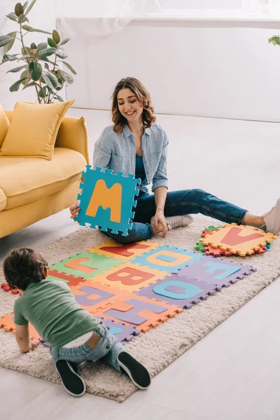 Lächelnde Mutter und Kind spielen mit Alphabet-Puzzlematte — Stockfoto