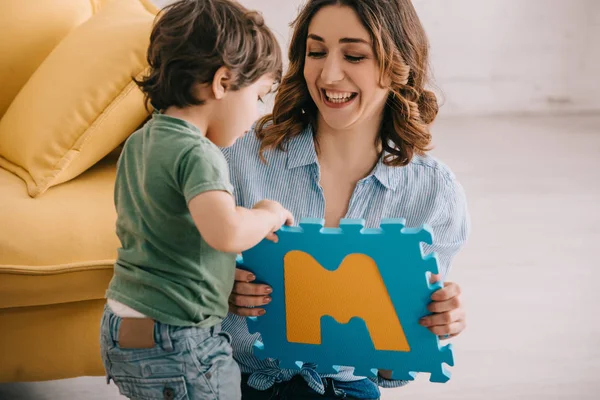 Sonriente madre aprendiendo cartas con su pequeño hijo en casa - foto de stock