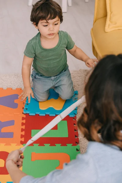 Vista cortada de mãe e filho com tapete de quebra-cabeça alfabeto na sala de estar — Fotografia de Stock