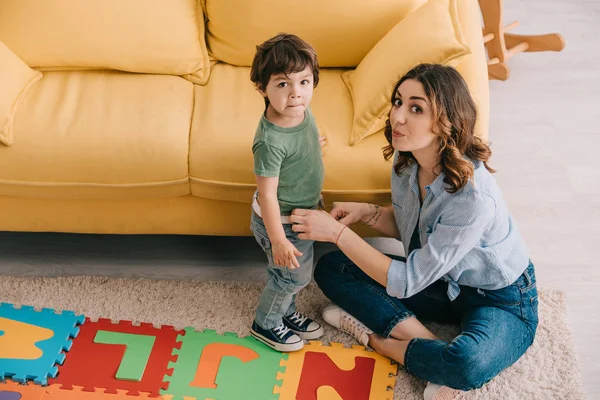 Madre e hijo con alfombra de rompecabezas alfabeto en la sala de estar - foto de stock