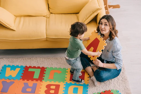 Sorridente madre e bambino che giocano con il tappetino puzzle alfabeto — Foto stock