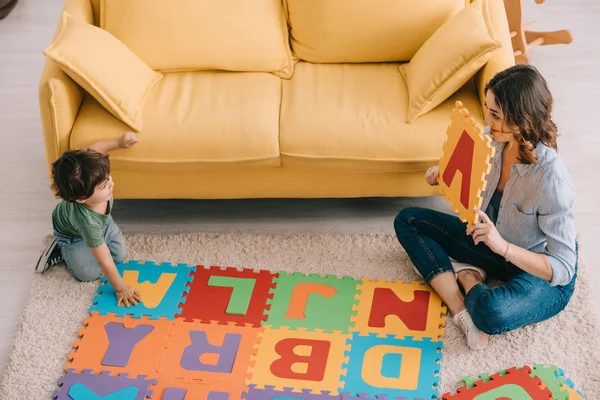 Vue aérienne de la mère et de l'enfant souriants jouant avec le tapis de puzzle alphabet — Photo de stock