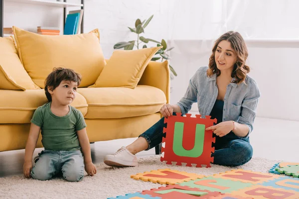 Sonriente madre y niño jugando con alfabeto alfombra del rompecabezas - foto de stock