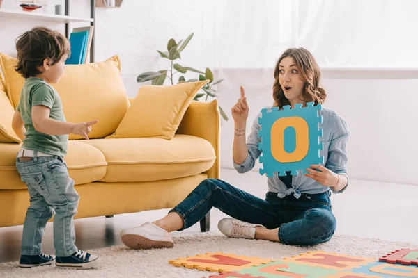 Emotionale Mutter zeigt Ideenschild beim Buchstabenlernen mit Sohn — Stockfoto