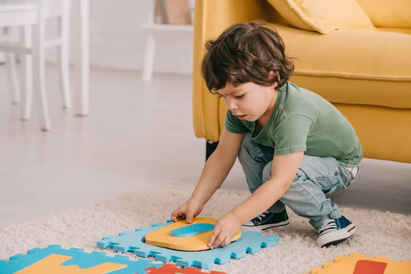 Niño concentrado en camiseta verde jugando con alfombra de rompecabezas - foto de stock