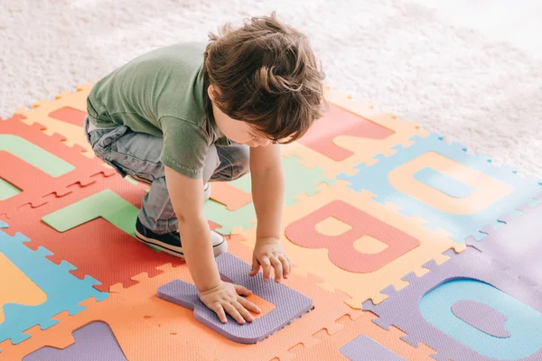 Cute child in green t-shirt playing with puzzle mat — Stock Photo