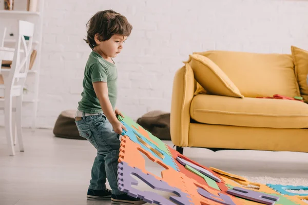 Vue complète de l'enfant en t-shirt vert jouant avec le tapis de puzzle — Photo de stock