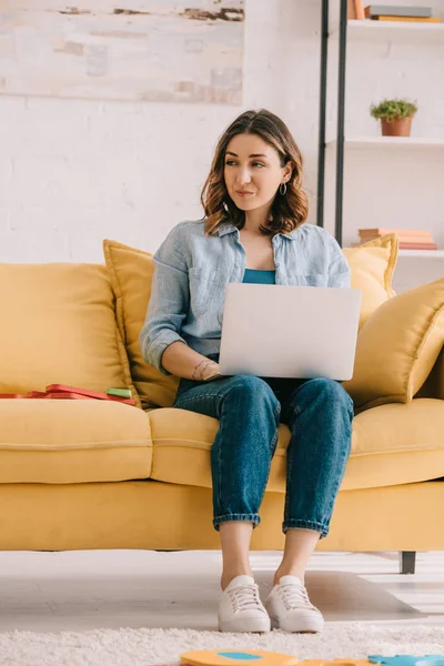 Attraktive Freiberuflerin auf gelbem Sofa sitzend und mit Laptop — Stockfoto