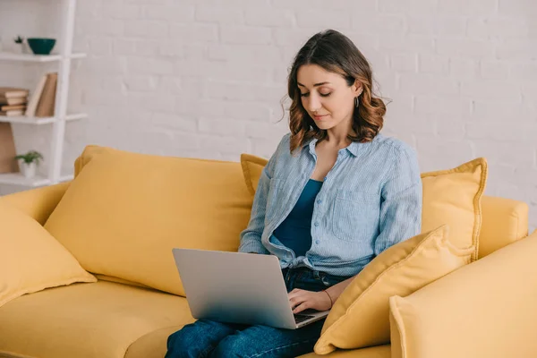 Attraktive Freiberuflerin auf gelbem Sofa sitzend und mit Laptop — Stockfoto