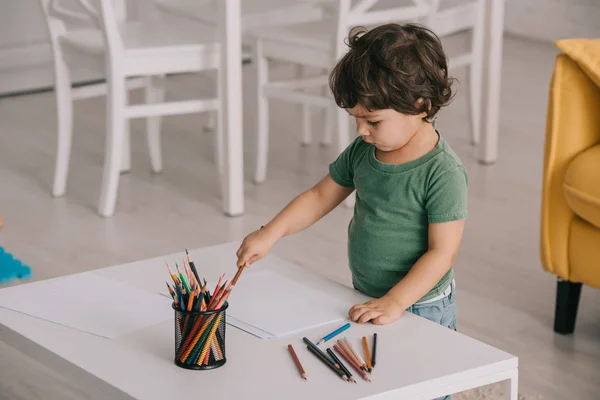 Enfant en t-shirt vert avec crayons de couleur et papiers dans le salon — Photo de stock