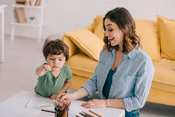 Madre e hijo emocionados dibujo con lápices de color en la sala de estar - foto de stock