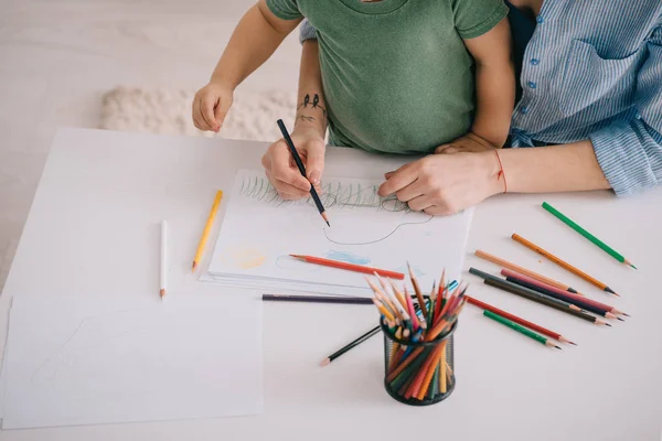 Cropped view of mother and son drawing with color pencils in living room — Stock Photo
