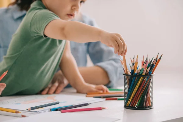 Vista recortada del dibujo de madre e hijo con lápices de color en la sala de estar - foto de stock