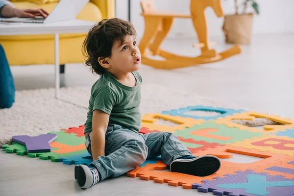 Neugieriges Kind in Jeans sitzt auf Puzzlematte mit Buchstaben — Stockfoto