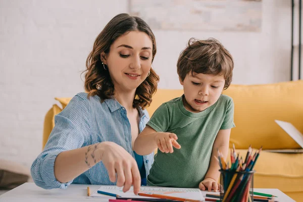 Madre e hijo dibujando con lápices de color en la sala de estar - foto de stock