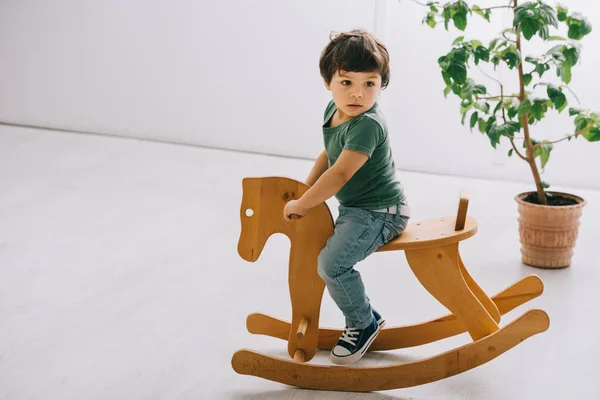 Cute child sitting on wooden rocking horse in living room — Stock Photo