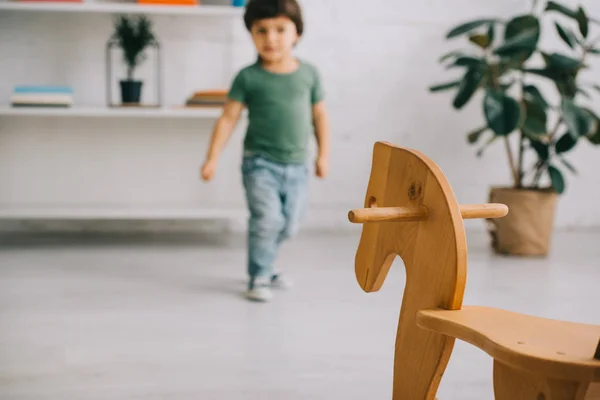 Focus sélectif de tout-petit garçon en t-shirt vert et cheval à bascule en bois — Photo de stock