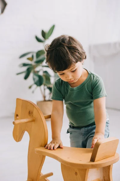 Bambino in t-shirt verde e cavallo a dondolo in legno — Foto stock