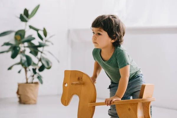 Criança bonito com cavalo de balanço de madeira na sala de estar — Fotografia de Stock