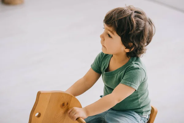 Bambino seduto su un cavallo a dondolo in legno in soggiorno — Foto stock