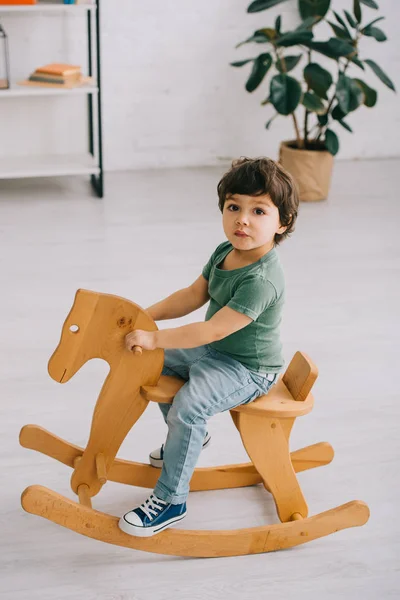 Kid sitting on wooden rocking horse in living room — Stock Photo