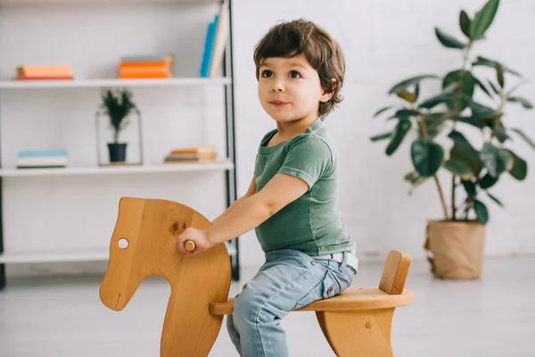 Criança sentada no cavalo de balanço de madeira na sala de estar — Fotografia de Stock