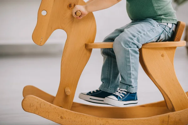 Cropped view of child sitting on wooden rocking horse in living room — Stock Photo