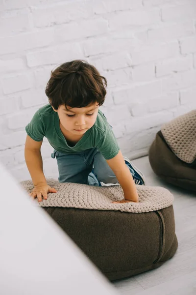 Niño en camiseta verde sentado en puf en el suelo - foto de stock