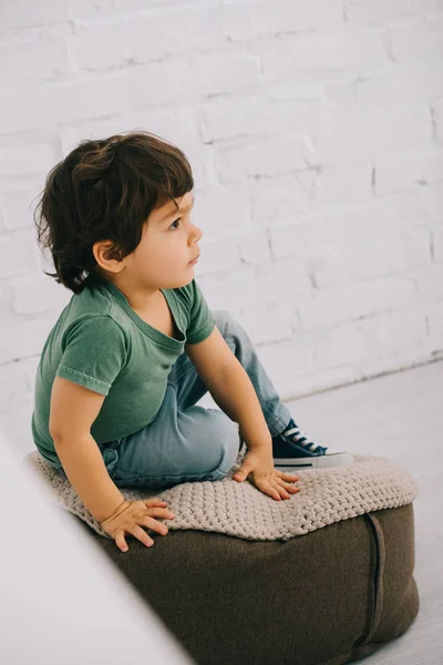 Child in green t-shirt sitting on pouf on floor — Stock Photo