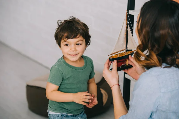 Mère montrant bateau jouet au petit fils en gree t-shirt — Photo de stock