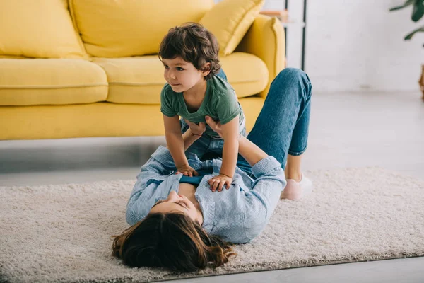 Happy mother and son playing on carpet in living room — Stock Photo