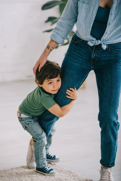 Niedliches Kind in grünem T-Shirt umarmt Mama im Wohnzimmer — Stockfoto