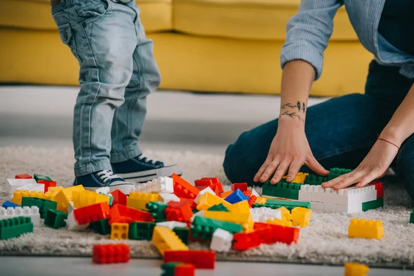 Vista recortada de madre e hijo jugando con lego en la alfombra en la sala de estar - foto de stock