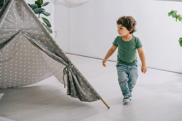 Vista a tutta lunghezza del bambino in jeans vicino al wigwam grigio — Foto stock