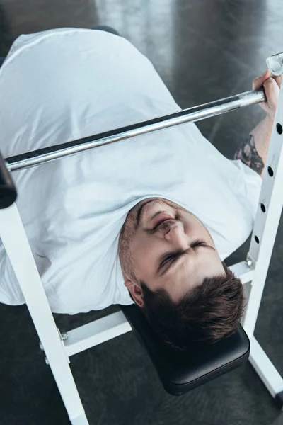 Hombre con sobrepeso en camiseta blanca haciendo ejercicio con barra en el gimnasio - foto de stock