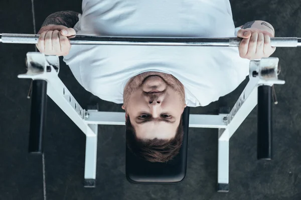 Vista superior del hombre con sobrepeso en camiseta blanca de entrenamiento con barra de pesas en el gimnasio - foto de stock