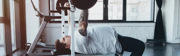 Panoramic shot of Overweight tattooed man training with barbell at gym — Stock Photo