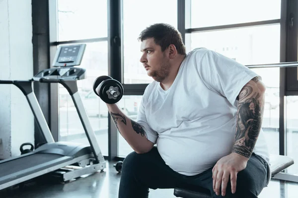 Overweight tattooed man exercising with dumbbell at sports center — Stock Photo