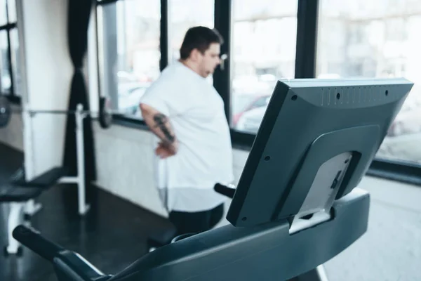 Messa a fuoco selettiva di tapis roulant e l'uomo in sovrappeso guardando attraverso la finestra al centro sportivo — Foto stock