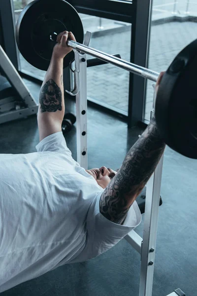 Overweight tattooed man training with barbell at gym — Stock Photo