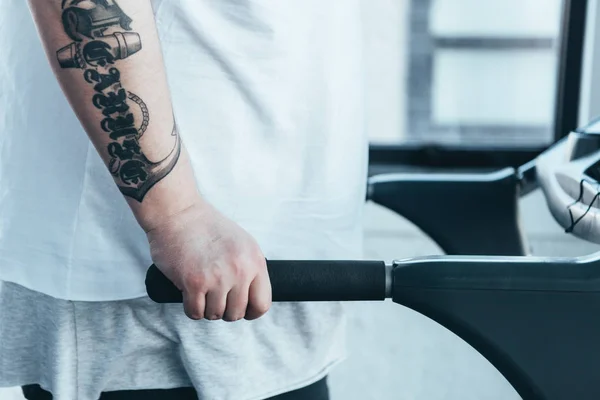 Cropped view of overweight tattooed man running on treadmill at sports center — Stock Photo