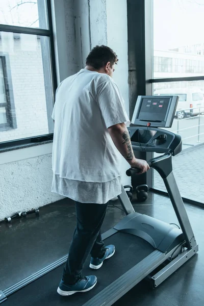 Rückansicht eines übergewichtigen tätowierten Mannes, der im Sportzentrum auf dem Laufband läuft — Stockfoto