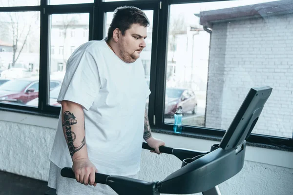 Overweight tattooed man running on treadmill at sports center — Stock Photo