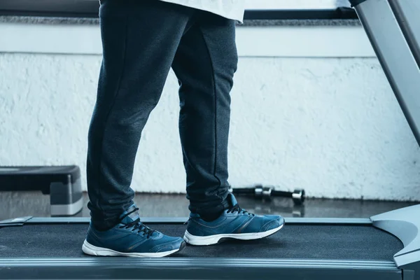 Cropped view of overweight man in trainers running on treadmill at sports center — Stock Photo