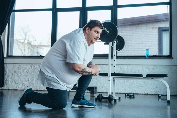 Hombre tatuado con sobrepeso en camiseta blanca que se extiende en el centro deportivo - foto de stock