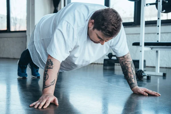 Overweight tattooed man doing push up exercise at sports center — Stock Photo