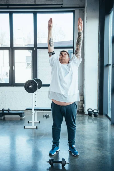 Overweight tattooed man in white t-shirt doing stretching exercise at sports center — Stock Photo