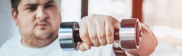 Tiro panorámico del hombre con sobrepeso mirando a la cámara mientras entrena con la mancuerna en el gimnasio - foto de stock