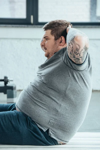 Übergewichtiger tätowierter Mann bei Sit-Up-Bewegung im Sportzentrum — Stockfoto